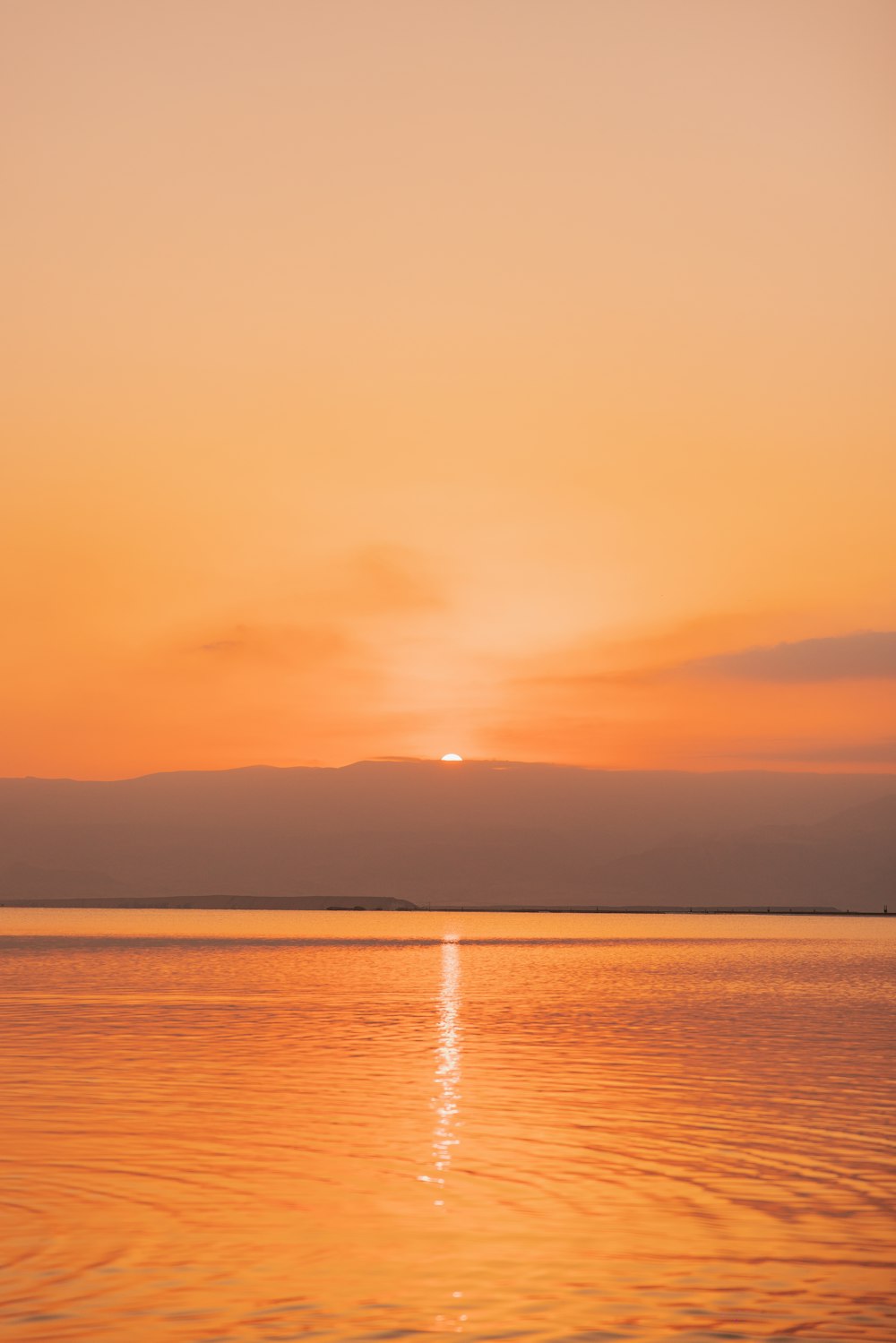 una gran masa de agua con una puesta de sol en el fondo