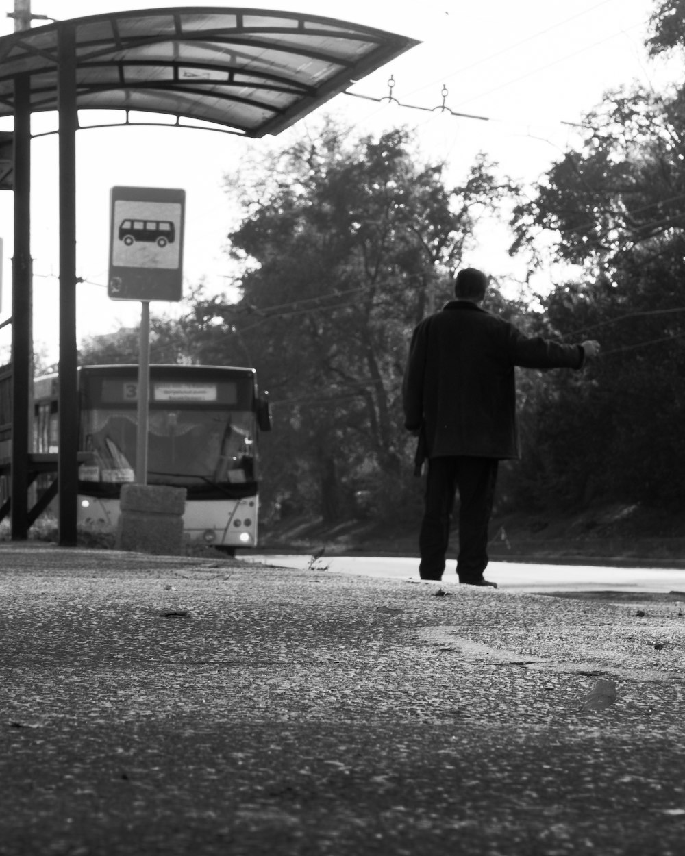 a black and white photo of a man waiting at a bus stop