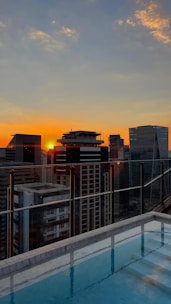 A modern condo building with a rooftop pool and panoramic city views at sunset.