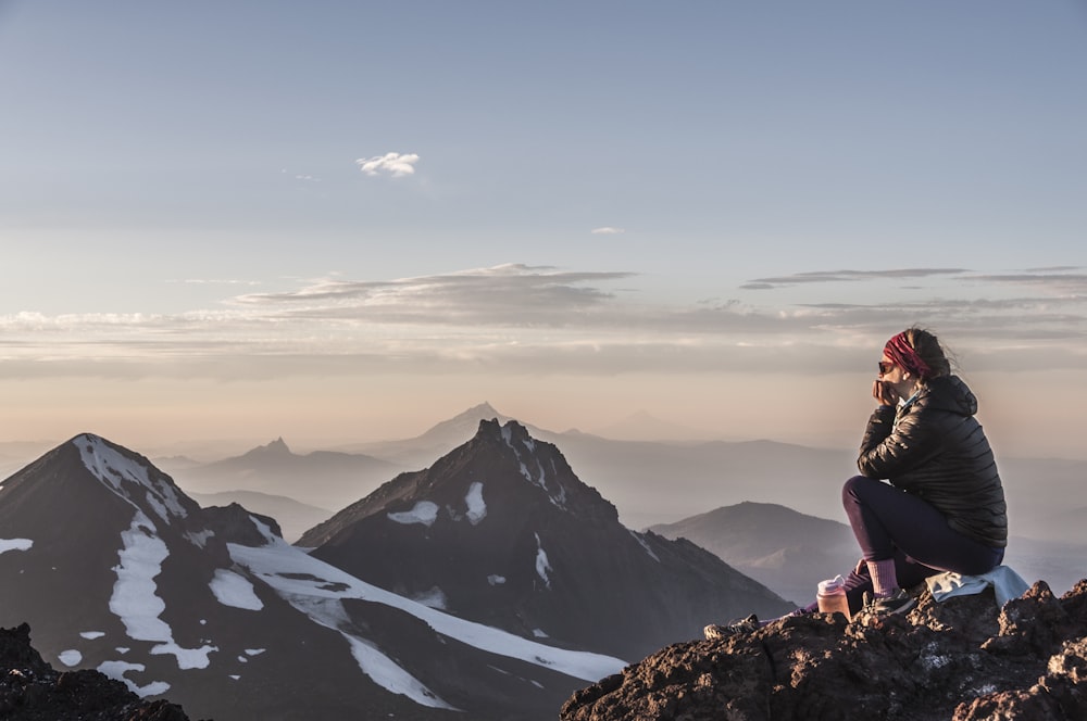 a woman sitting on top of a mountain next to snow covered mountains