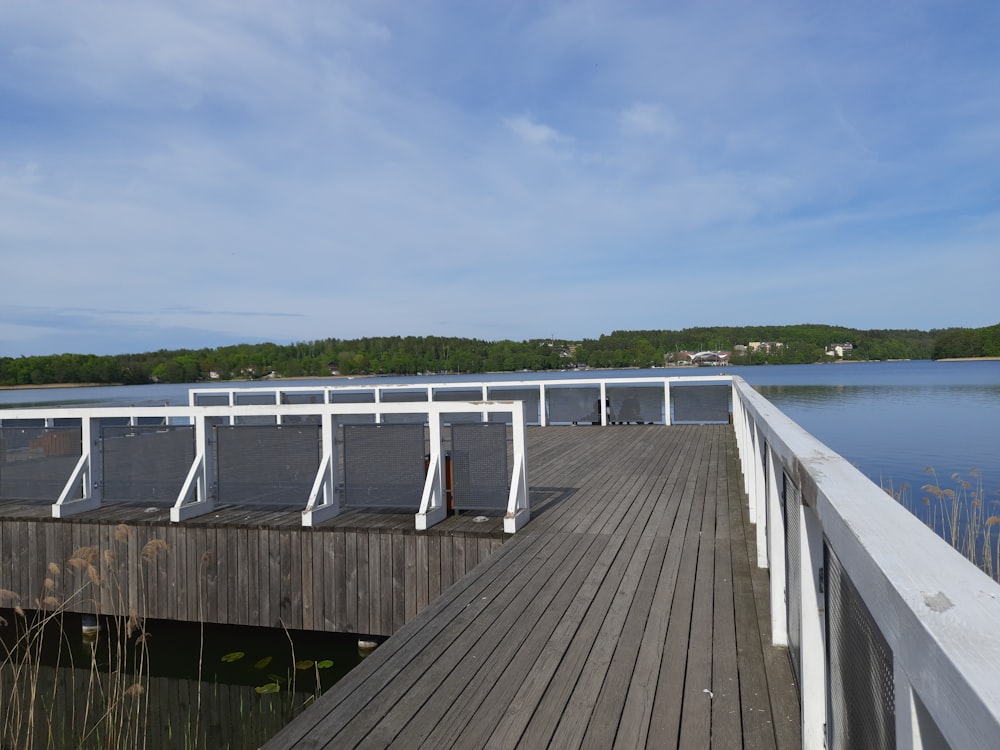 a wooden dock with chairs on it next to a body of water