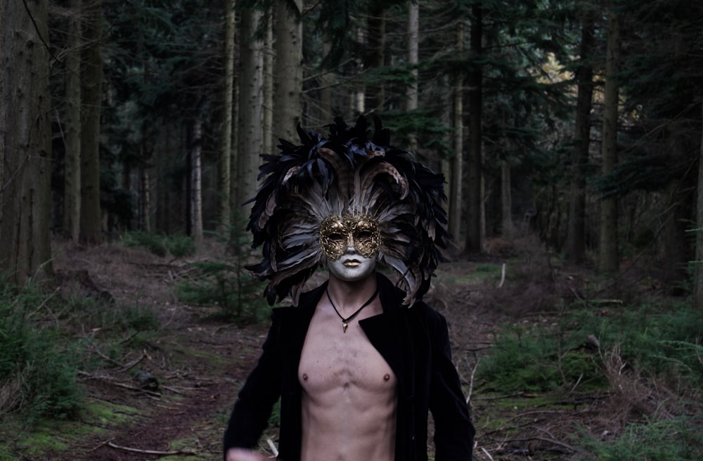 a man with a mask and feathers on his head walking through a forest