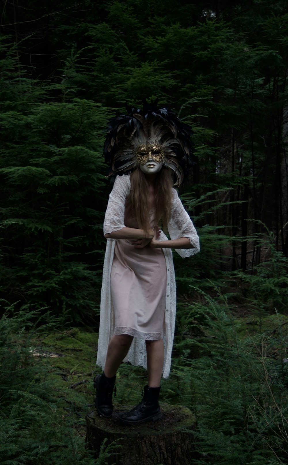 a woman with a mask on standing on a stump in the woods