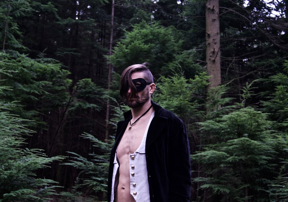 a shirtless man standing in front of a forest