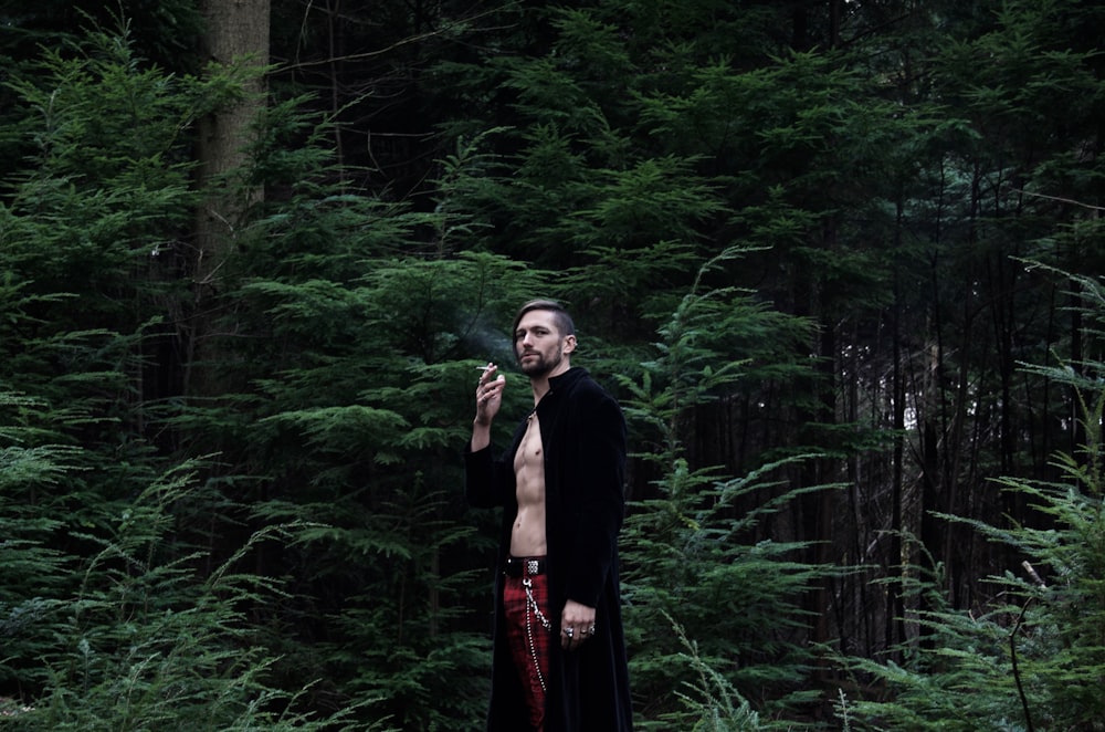 a man standing in a forest smoking a cigarette