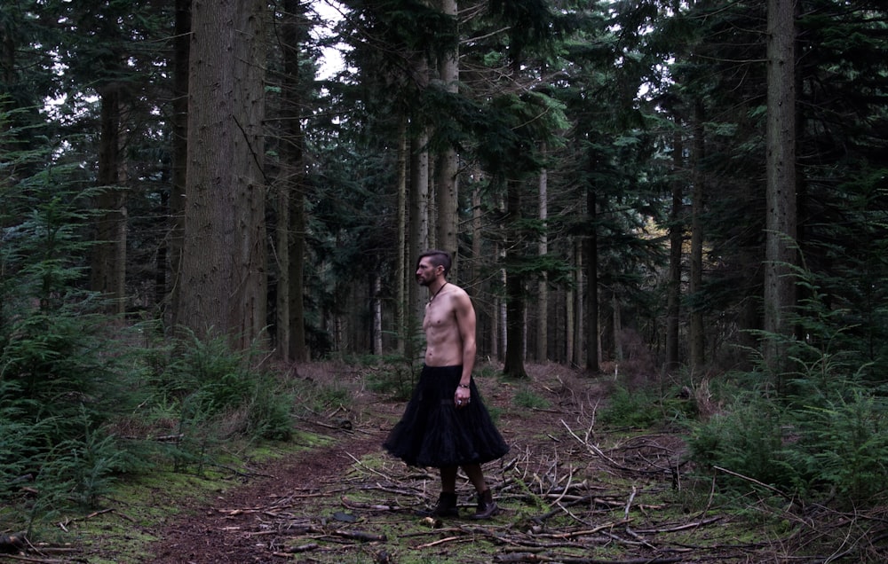 a shirtless man standing in the middle of a forest