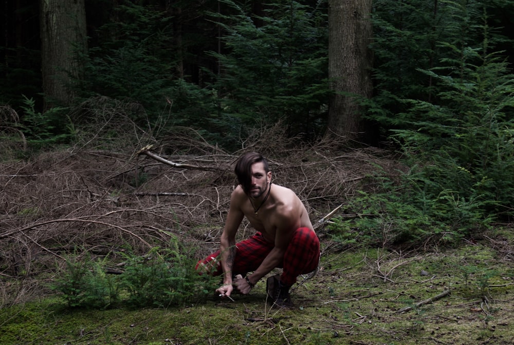 a shirtless man kneeling down in the woods
