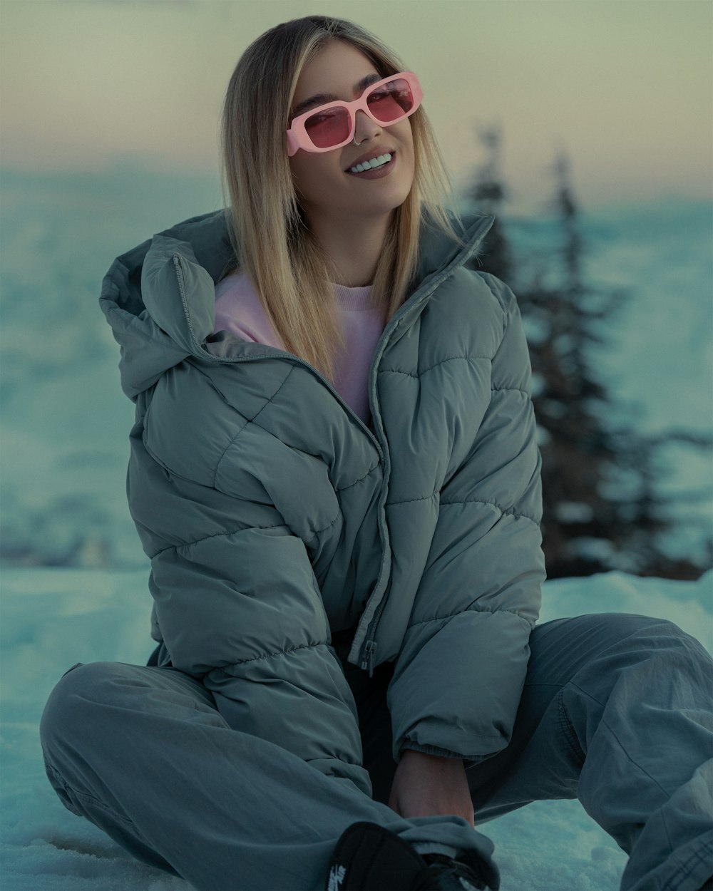 a woman sitting in the snow wearing sunglasses