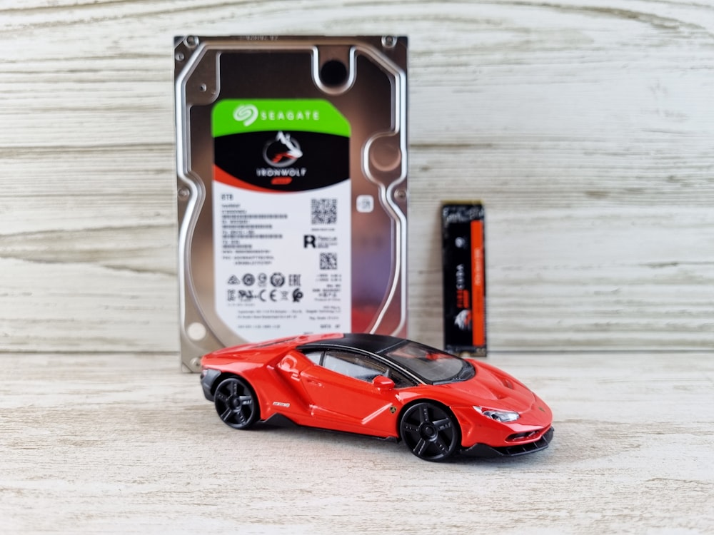 a red toy car sitting in front of a hard drive