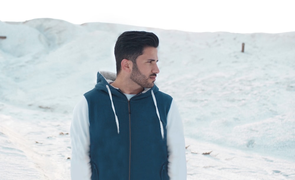a man standing in the snow wearing a blue and white hoodie