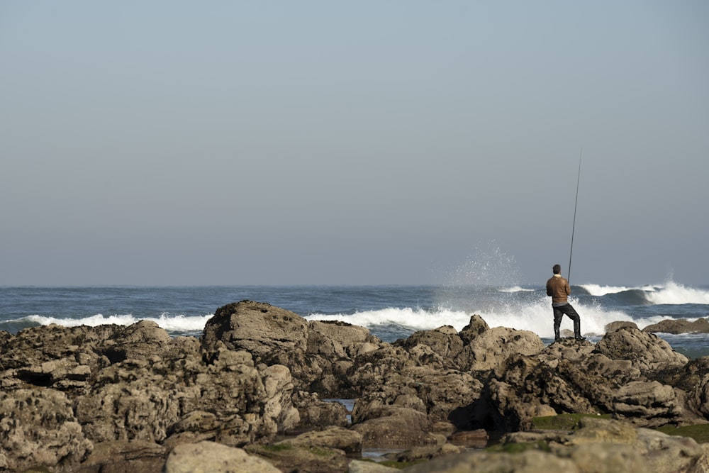 a man fishing on a rocky beach next to the ocean