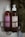 Two pump bottles of hair care products are placed in a black wire shower caddy. The bottle on the left has a purple label and contains conditioner, while the bottle on the right has a cream label and contains shampoo. Both bottles are branded 'Ceremonia' and have a minimalist design. The background is slightly blurred, featuring leaves.