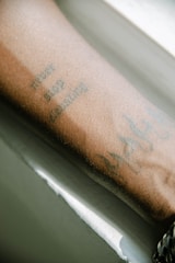 An arm adorned with tattoos, including text and other designs, resting against a white background.