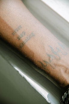 An arm adorned with tattoos, including text and other designs, resting against a white background.