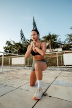 a woman in a sports bra top and shorts squatting on a tennis court