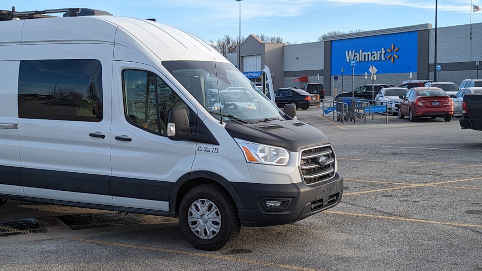 A sleek c.a.r.e. branded passenger van parked at the Walmart pickup zone under a clear blue sky.