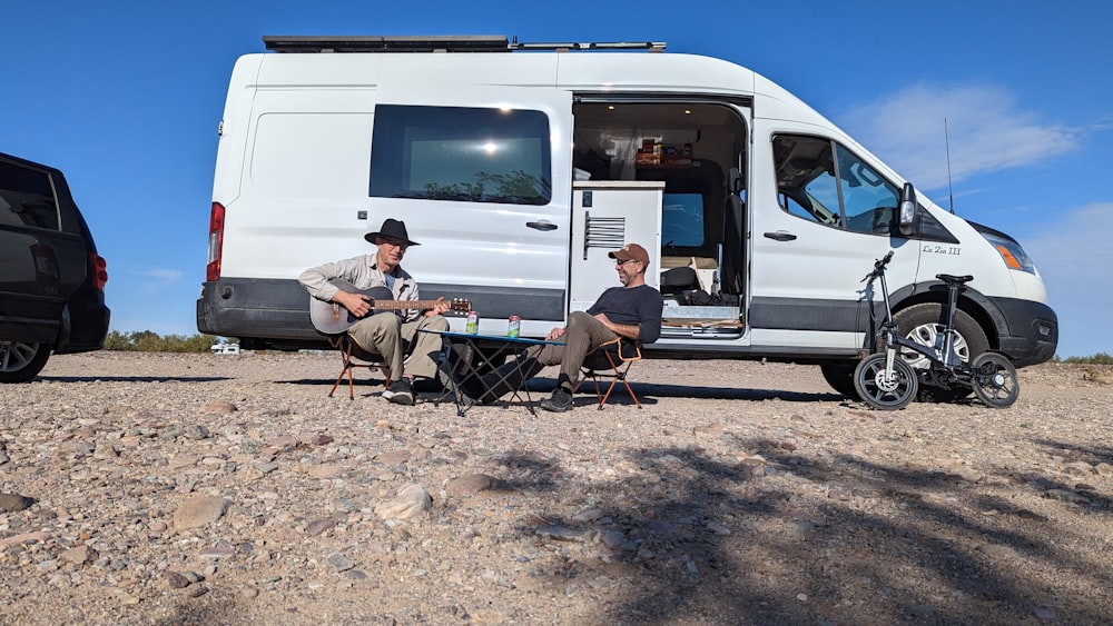 two men sitting at a table in front of a van