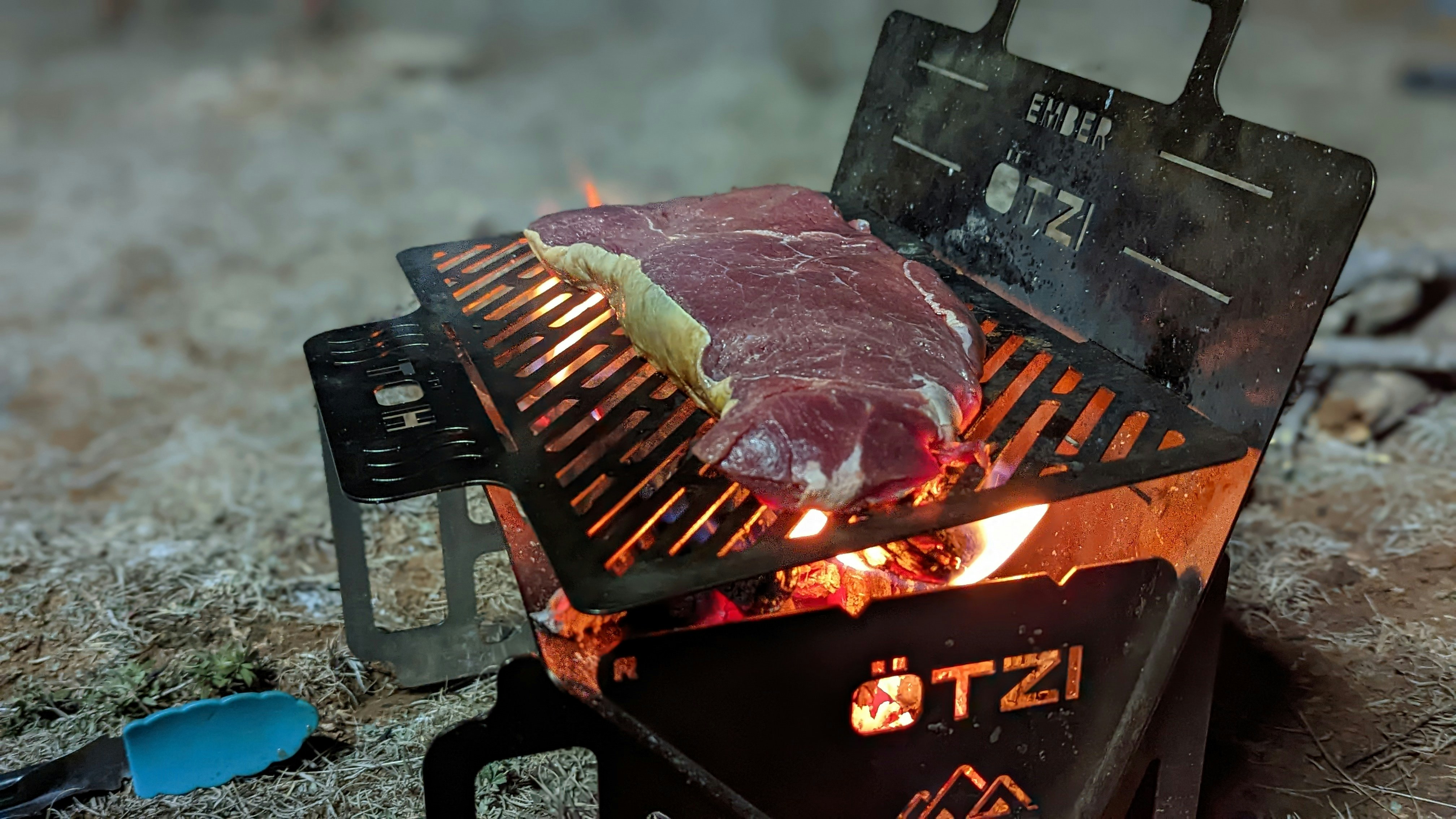 Un bistec se está cocinando en una parrilla en el suelo