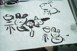 Ink drawings and calligraphy on paper featuring cartoon-like rabbits alongside traditional Chinese characters. The artwork appears hand-painted, displaying variations in brushstroke thickness and ink saturation.