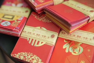 Stacks of decorative red envelopes, often associated with celebrations and traditional Chinese festivals. The envelopes are embellished with gold designs and Chinese characters, giving them a festive appearance.