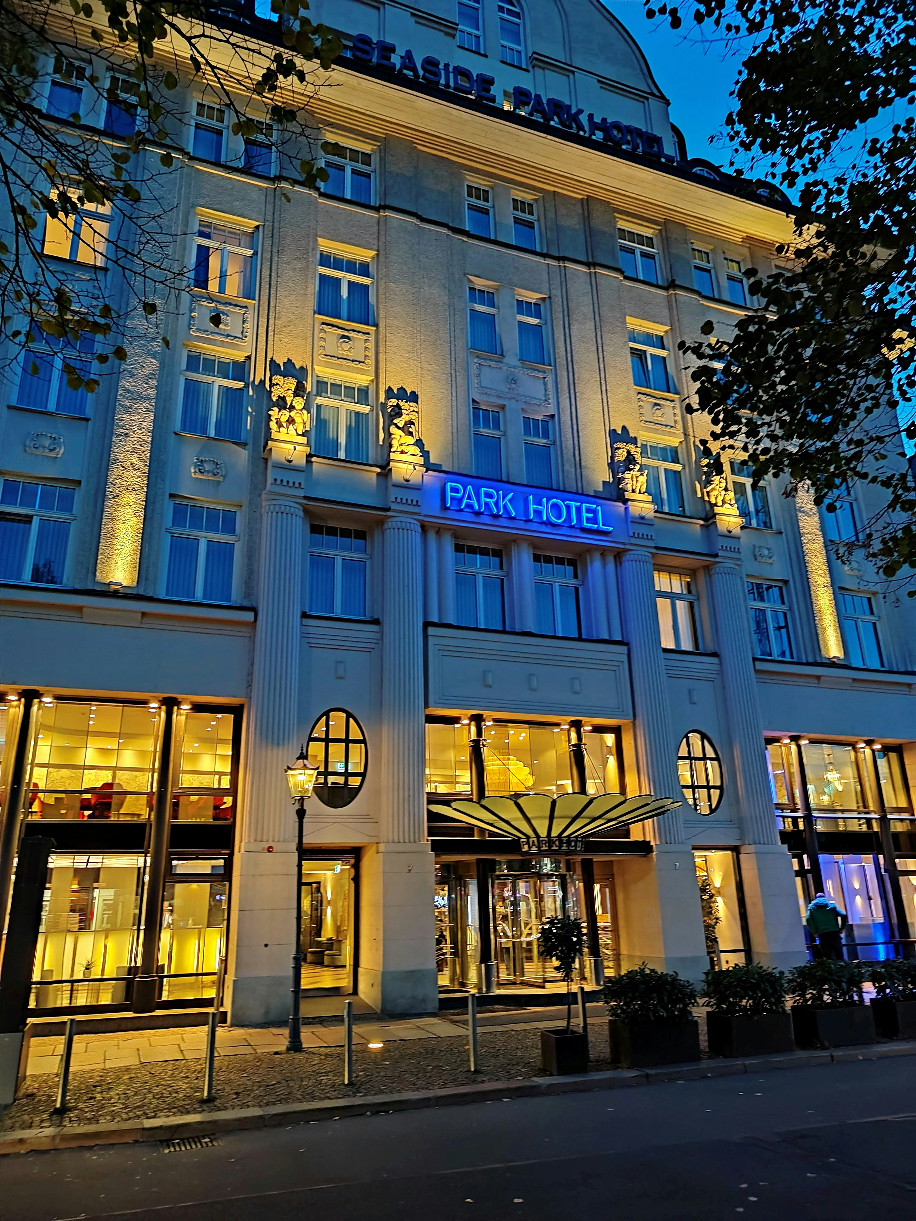 Hotel exterior at dusk with warm lit windows and a quiet driveway in soft blue light