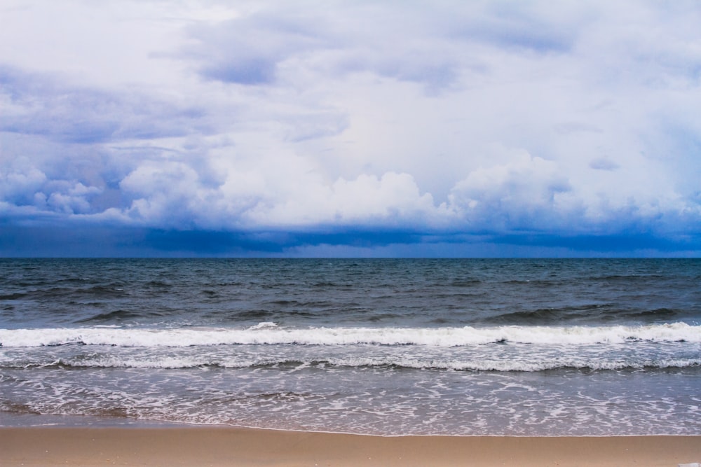 a beach with waves coming in to shore under a cloudy sky
