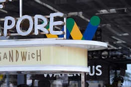 Neon and painted signs with blurred words and letters. Includes words like 'SANDWICH' and partial letters of another word. The backdrop features different-painted designs of letter W in green, blue, and yellow colors.