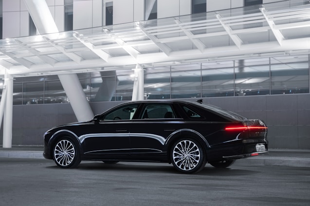 A sleek black luxury sedan parked outside a modern airport terminal, ready to welcome passengers.