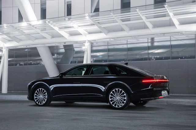 A sleek black luxury sedan gleaming under bright city lights, parked in front of a modern glass building.