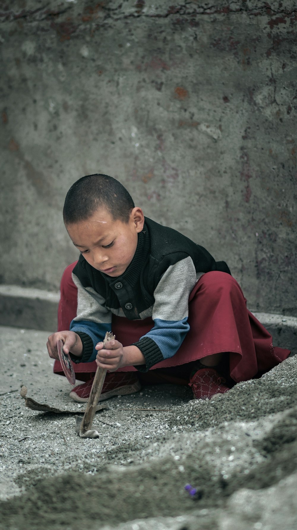 a young boy sitting on the ground holding a knife