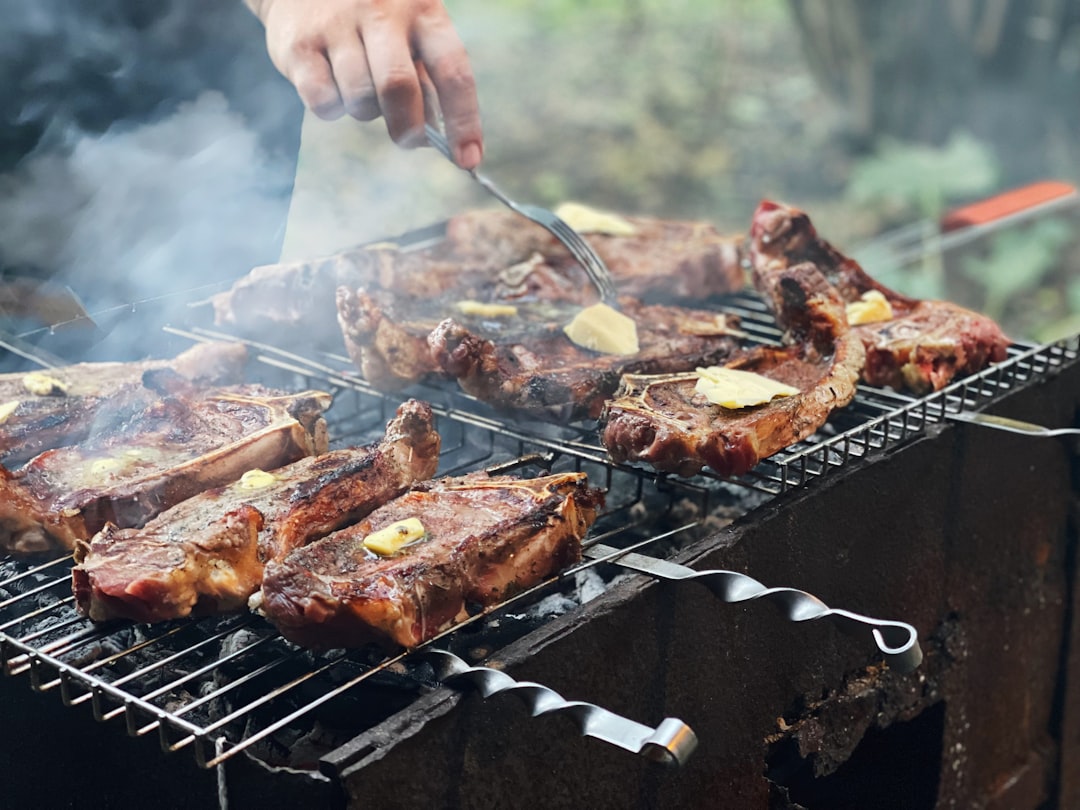 a person is cooking steaks on a grill, Open air stakes
