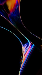 An abstract digital artwork featuring swirling, colorful patterns against a dark background. The composition includes vibrant hues of blue, orange, pink, and yellow with smooth, flowing curves that suggest fluid motion.