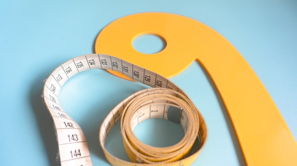 A yellow curved measuring tool lies on a light blue background alongside a white measuring tape with black markings, neatly coiled.