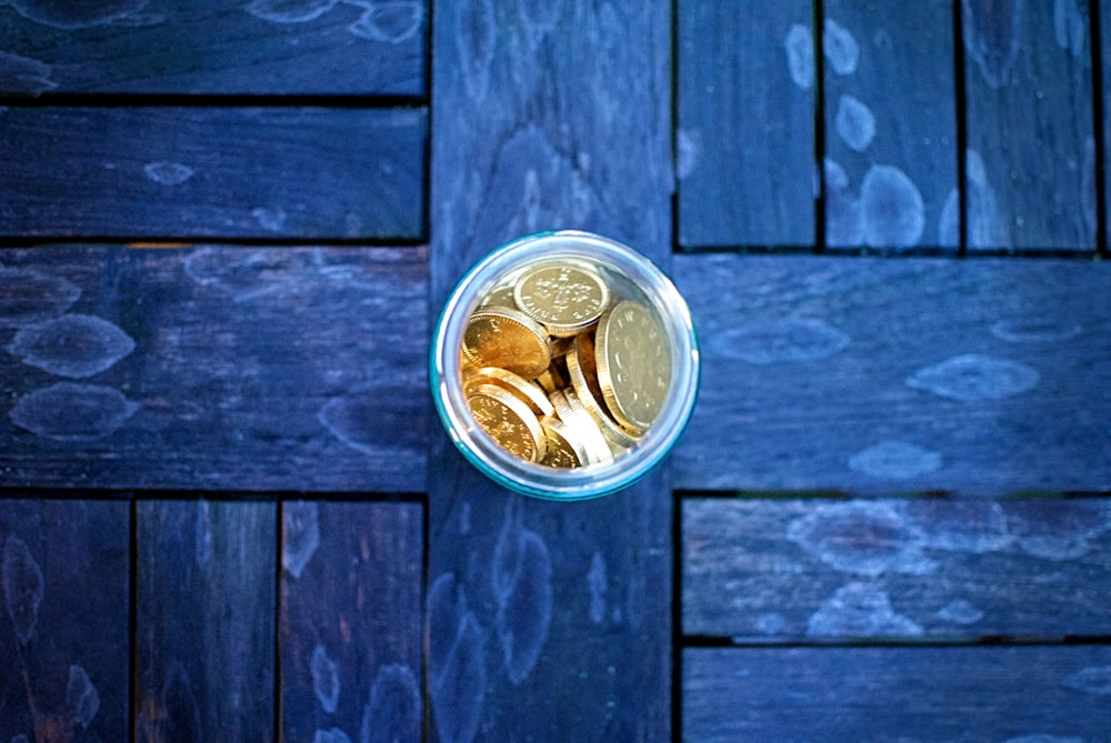 a glass filled with coins sitting on top of a wooden floor