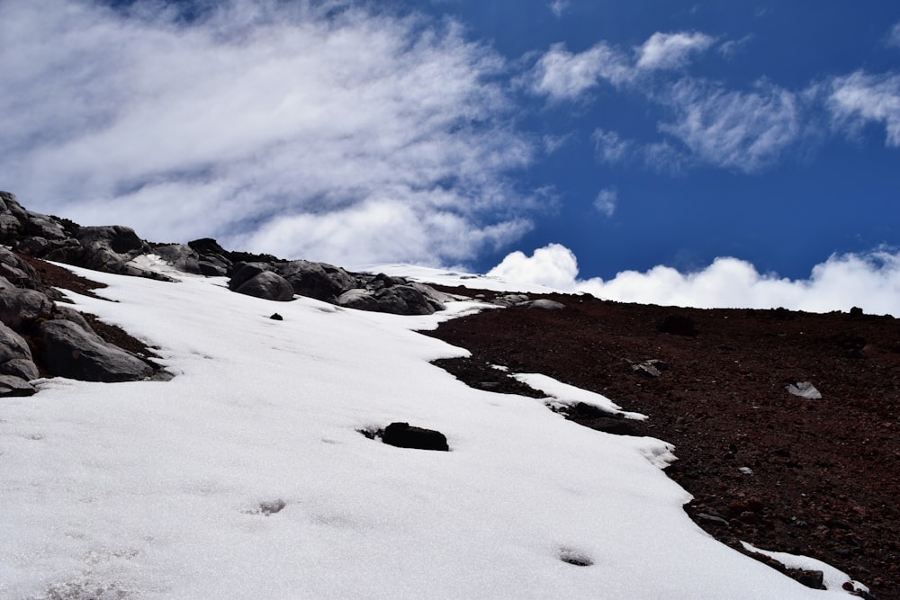 a snow covered hill with rocks and clouds in the background