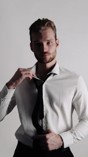 A groom adjusting his tie with a calm and thoughtful expression in a minimalist setting