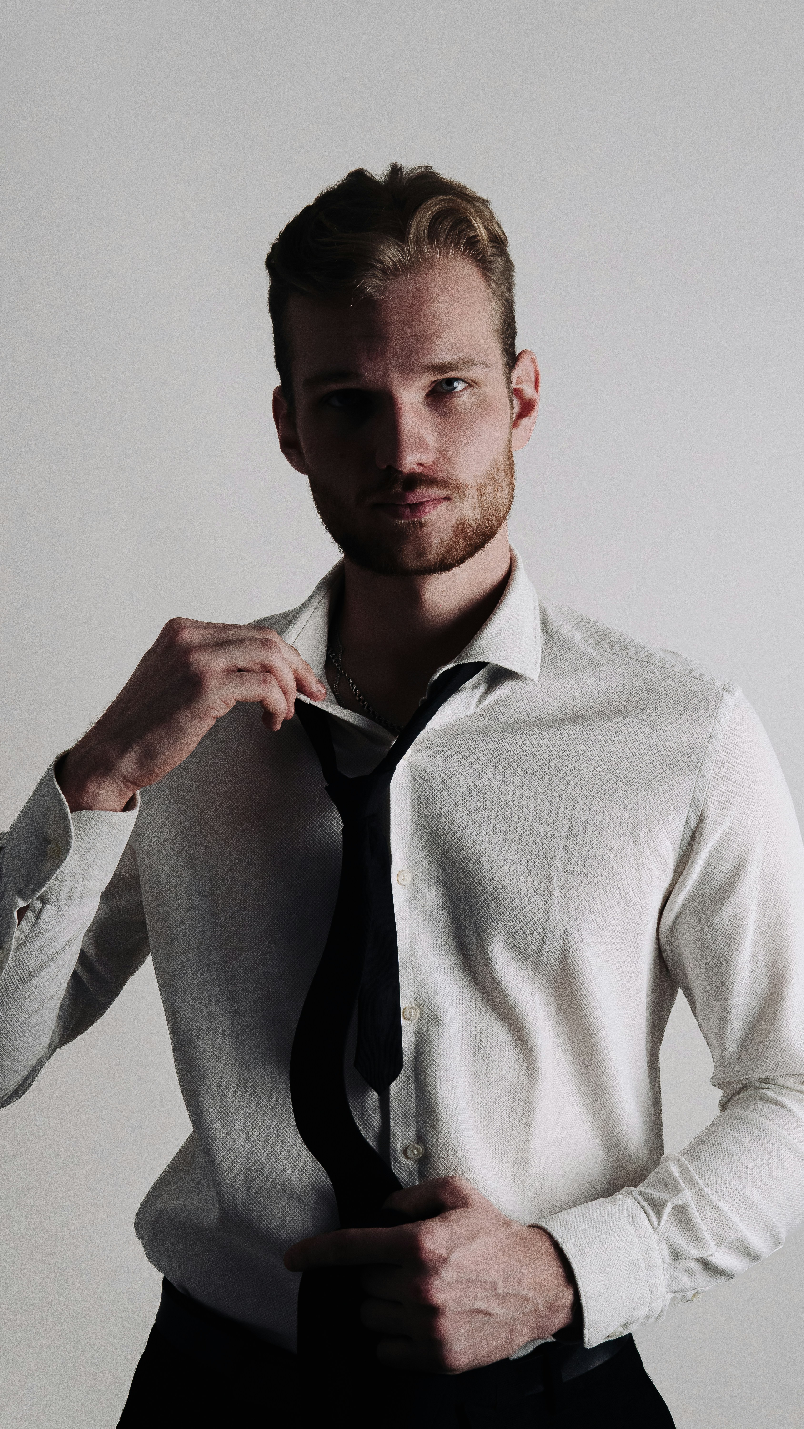 A man, a businessman in a shirt and tie takes off his tie