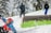 A skier in a bright blue and red outfit is navigating a snow-covered slope. The person appears to be in motion, with snow spraying around them. In the background, two other individuals dressed in winter gear are standing with skis, surrounded by snow-draped trees.