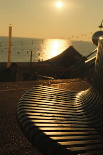 A sleek minimalist metal bench bathed in golden sunset light on a wooden deck.