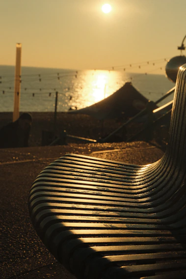 A sleek minimalist metal bench bathed in golden sunset light on a wooden deck.