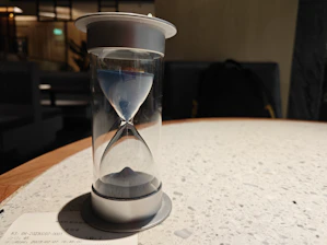 Close-up of a linen-bound diary beside a black sand hourglass on a wooden table.