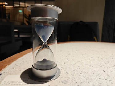 Close-up of a linen-bound diary beside a black sand hourglass on a wooden table.