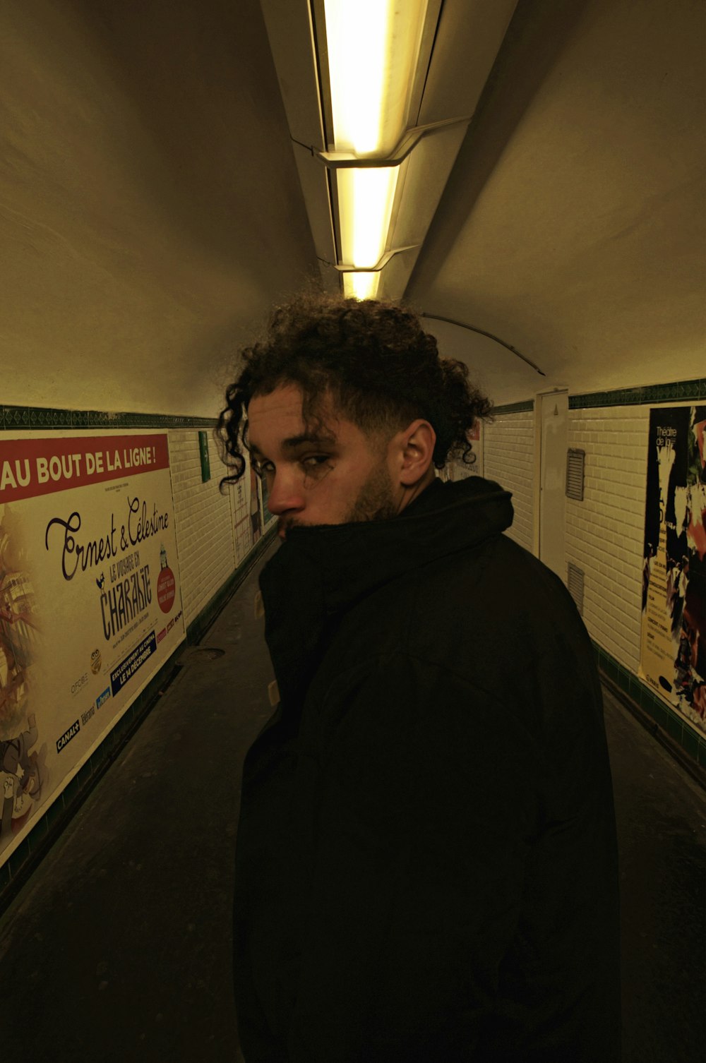 a man with curly hair standing in a tunnel