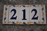 A set of decorative tiles displaying the number 212 against a textured stone background. The tiles feature ornate floral patterns in yellow and blue around the numbers.