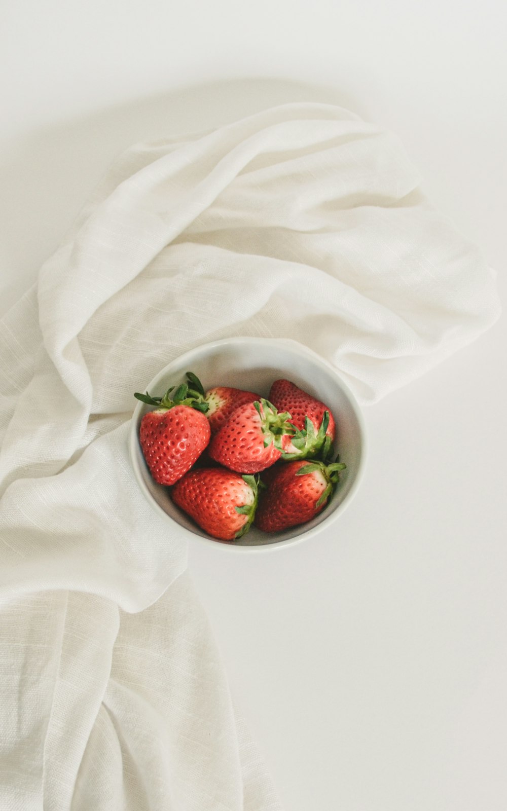 a bowl of strawberries sitting on top of a white cloth