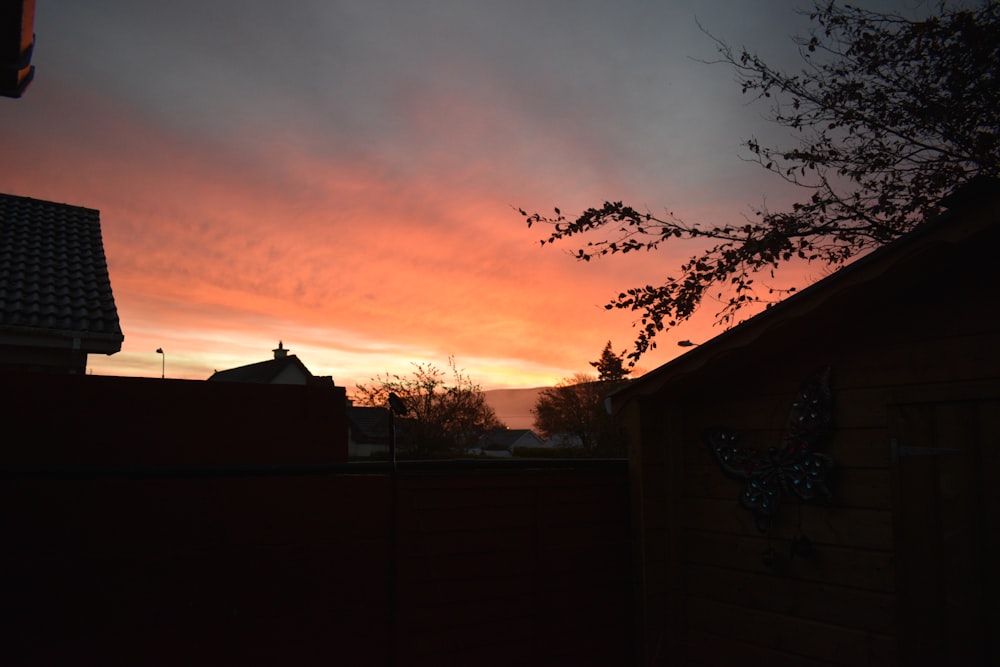 the sun is setting behind a house with a tree in the foreground