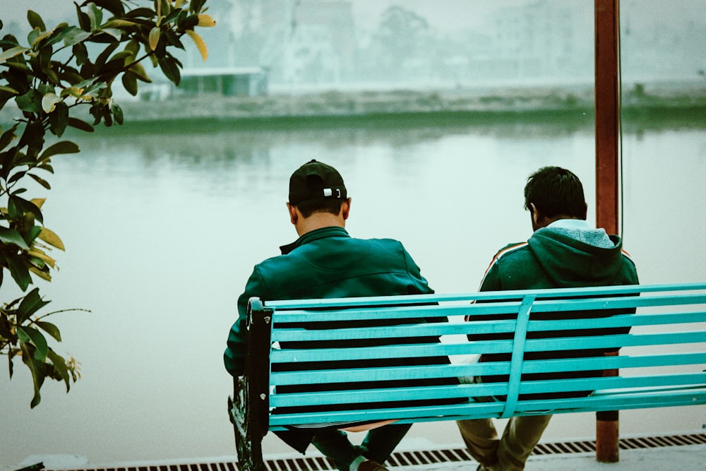 a couple of men sitting on top of a blue bench