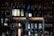 A variety of wine and champagne bottles are neatly arranged on dark wooden shelves. The scene is set in dim lighting, highlighting the bottles and emphasizing the labels. The background is slightly blurred, putting focus on the bottles themselves.