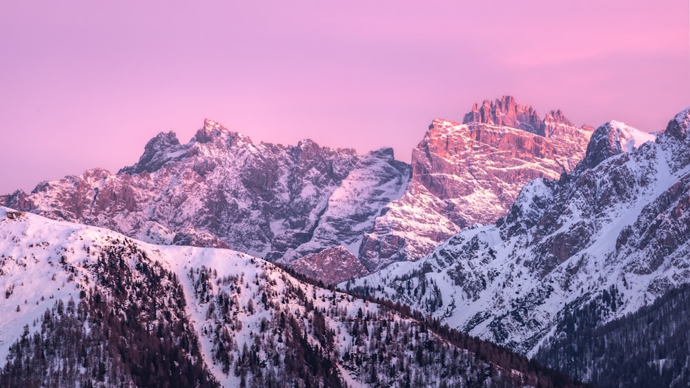 a mountain range covered in snow at sunset