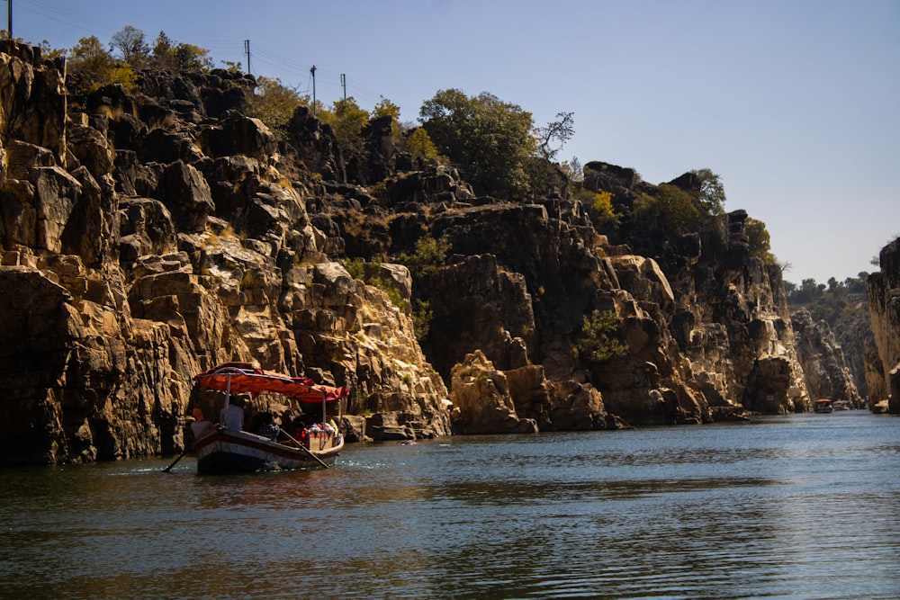 a boat floating on top of a river next to a rocky cliff